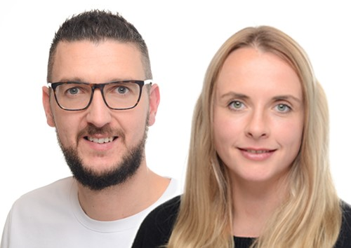 distriko Katharina Oliver Katharina hat blonde lange Haare und grüne Augen. Oliver hat dunkle kurze Haare, einen Bart und trägt eine Briille. Sie sind das Team von distriko und lächeln in die Kamera.