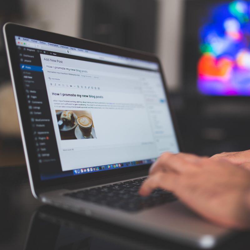 WordPress Blogger Ein WordPress Blogger hat ein Apple Macbook auf einem schwarzen Tisch stehen und schreibt einen Blog-Beitrag über Kaffee und Kuchen