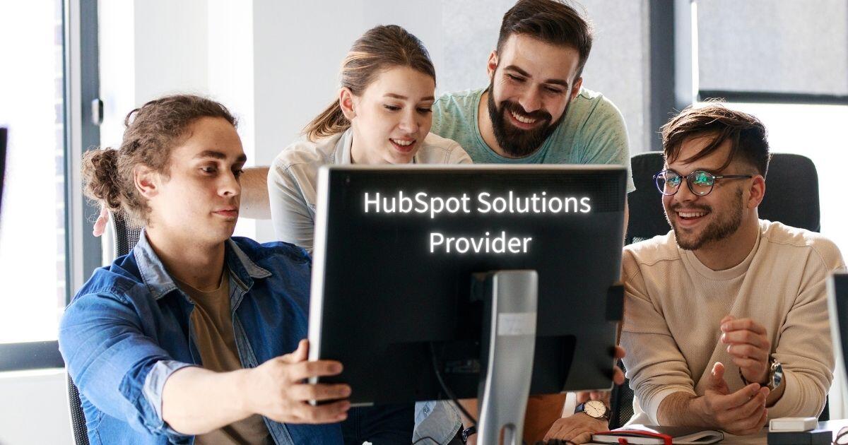 Ein Team von 4 Personen schaut gemeinsam in einen Bildschirm. Auf der Rückseite des Monitors steht HubSpot Solutions Provider geschrieben