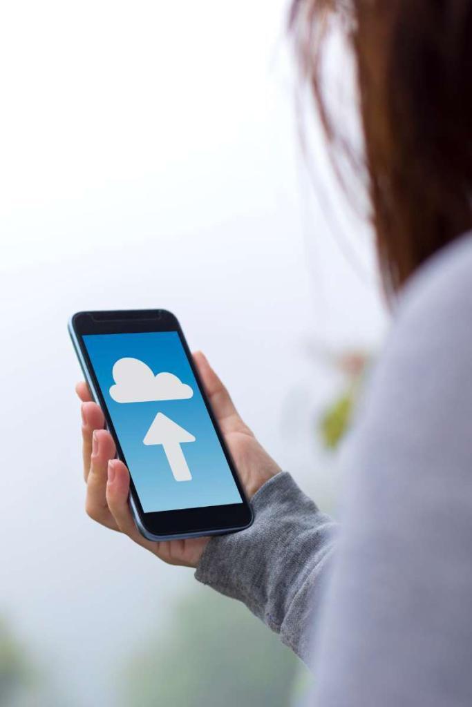 Eine Frau hält ein Smartphone in der Hand, auf der ein Pfeil zu einer Wolke in den blauen Himmel zeigt.