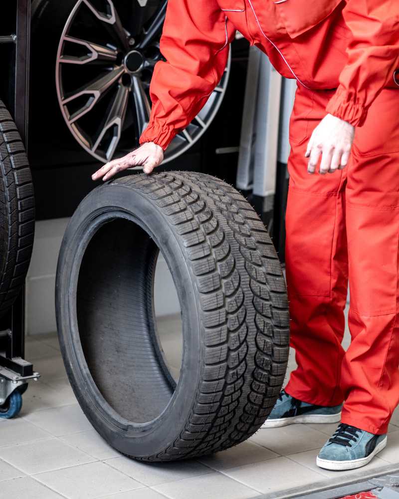 Ein Monteur im roten Overall hält die rechte Hand auf einen demontierten Reifen.