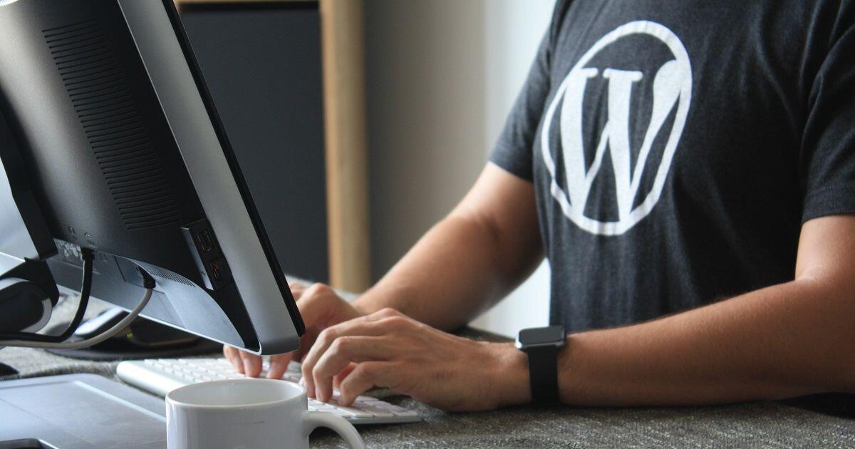 Ein Webdesigner mit blauem T-Shirt sitzt am Schreibtisch und arbeitet daran, dass WordPress barrierefrei wird.