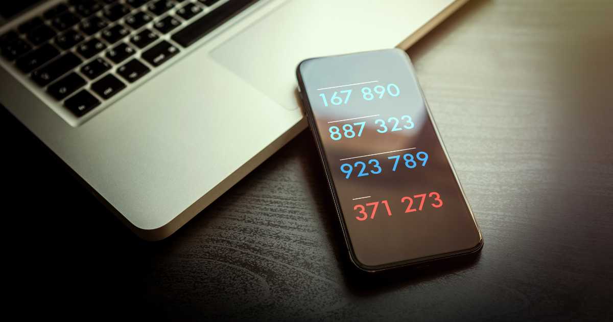 Auf der Kante von einem Macbook liegt ein Smartphone mit 4 verschiedenen Zahlencodes als Zwei Faktor Authentifizierung