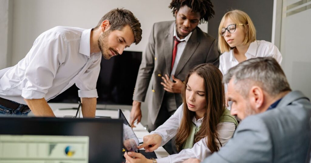 Fünf Personen beraten sich in einem Büro und betrachten gemeinsam Inhalte auf einem Tablet.